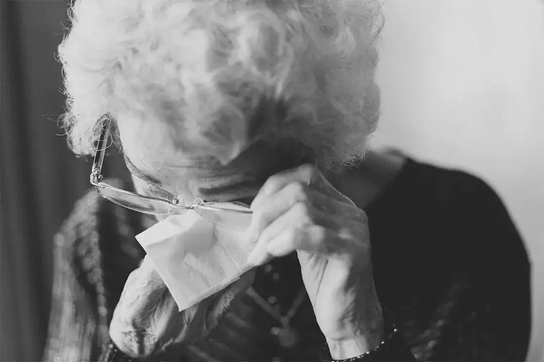 Black and white picture of elderly lady wiping her tears