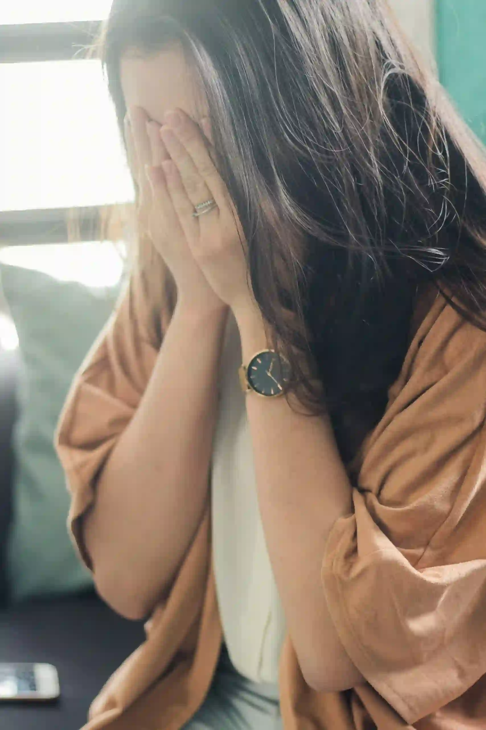 Young woman with long hair hiding her face with her hands