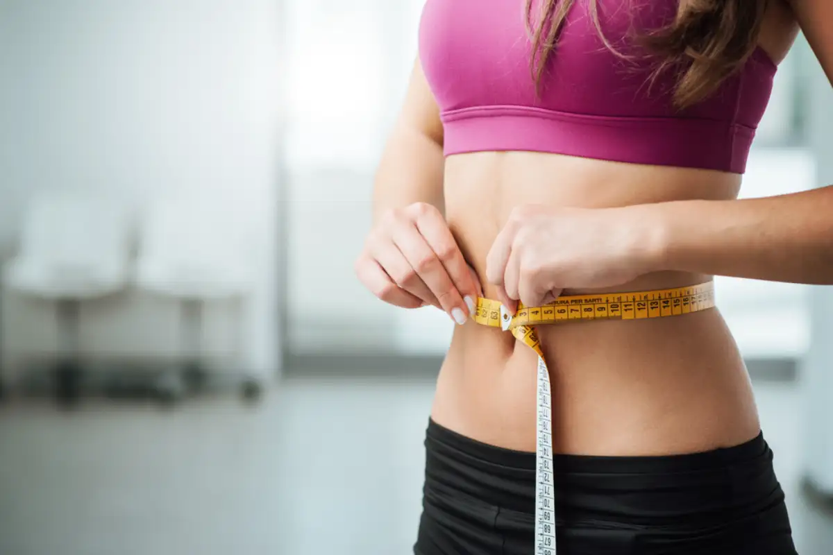 Slim young woman measuring her thin waist with a tape measure